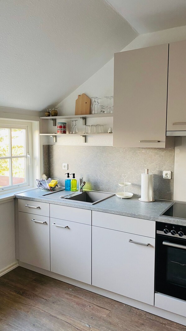 Una cocina moderna con armarios blancos, horno integrado y ventana que proporciona luz natural.