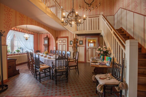 Comedor con una gran mesa, sillas, un candelabro y una escalera.