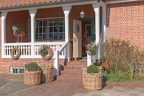 Ein Backsteinhaus mit einer Veranda, zwei Korbmöbelkörbe mit Pflanzen und einer Tür.