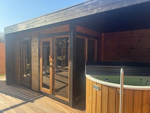 Una terraza de madera con un jacuzzi y una zona cubierta con puertas de cristal.