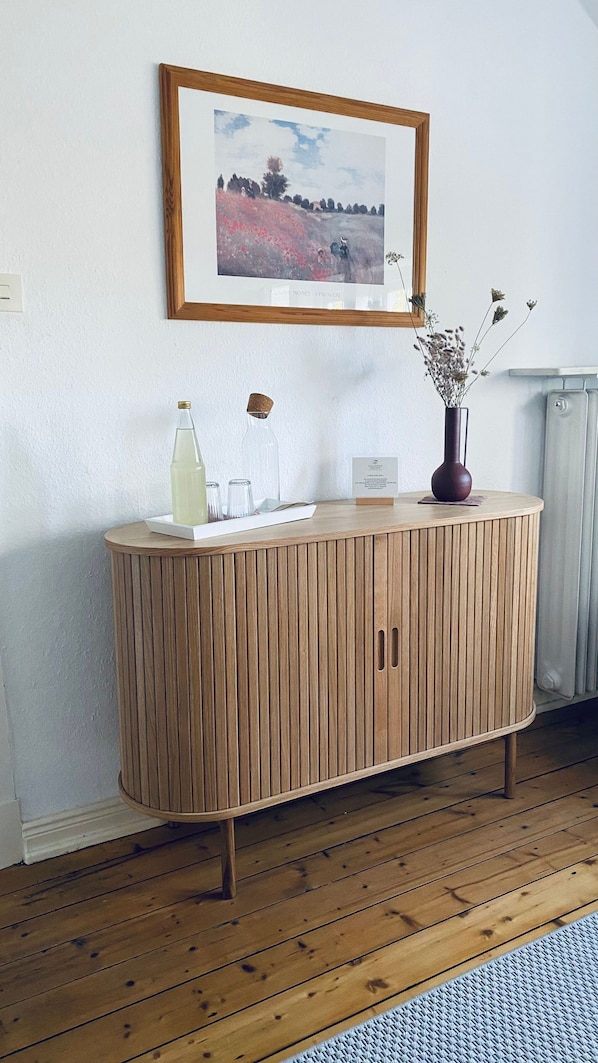 Ein Holzschrank mit einem Rahmenbild darüber, einer Vase mit Trockenblumen und einer Flasche auf der Oberfläche.