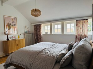 Ein Schlafzimmer mit Bett, Heizkörper, einem Fenster mit Vorhängen und einer Pendelleuchte.