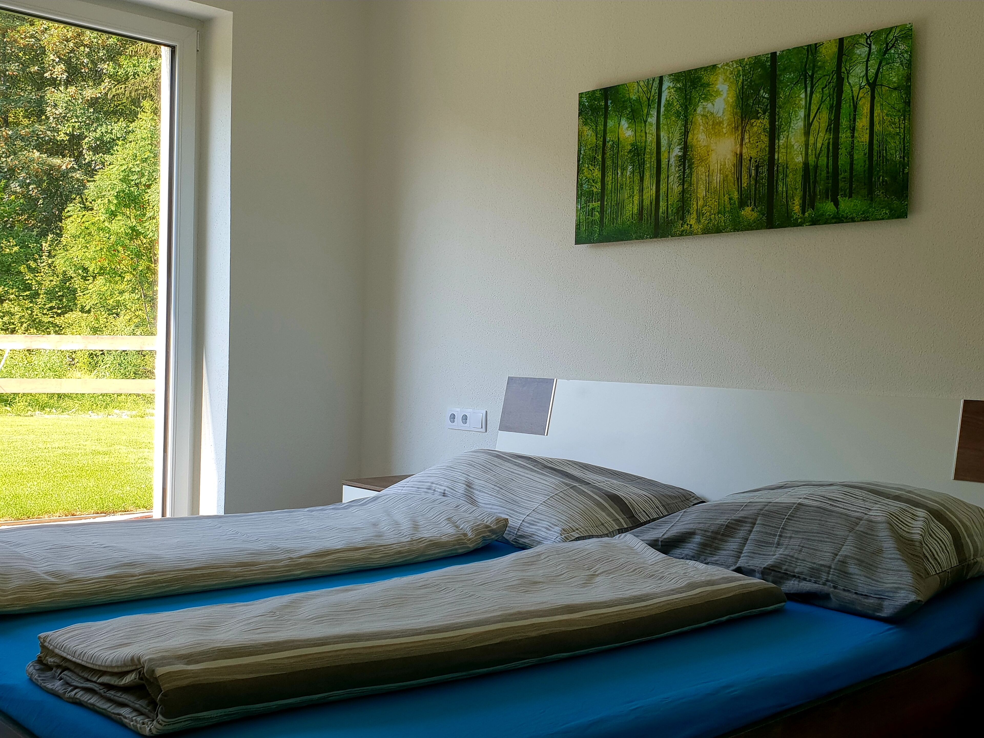 Ein Schlafzimmer mit einem Bett, einem Fenster und einem Waldgemälde.