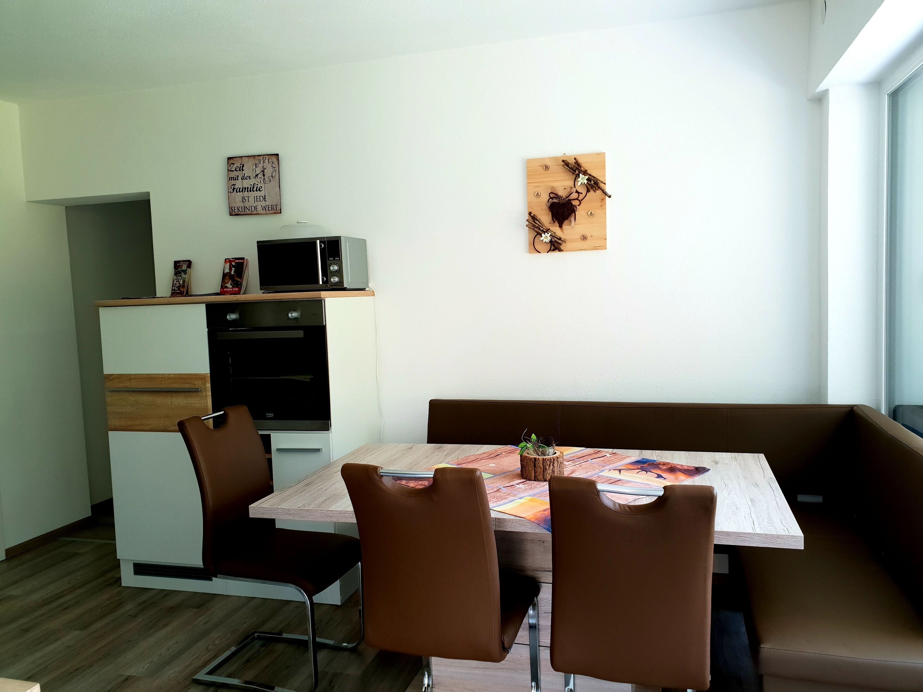 Un espace repas moderne avec une table en bois, des chaises en cuir marron, un four encastré et un micro-ondes posé sur le dessus.