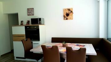 Un espace repas moderne avec une table en bois, des chaises en cuir marron, un four encastré et un micro-ondes posé sur le dessus.