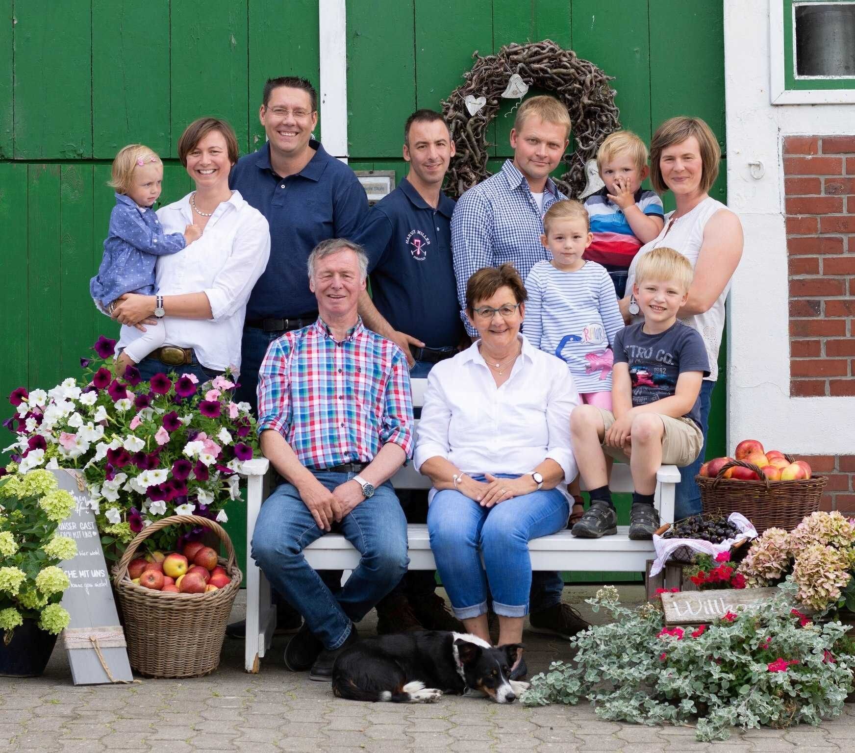 A group of people seated on a bench in front of a green building with a wreath and flowers.