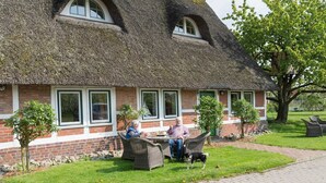 A thatched-roof building with a brick facade, outdoor seating, and a small tree in the foreground.