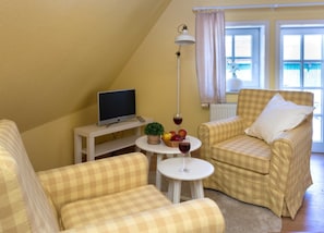 A cozy room with a checkered sofa, a small table with a plant and fruit, and a television on a white stand.