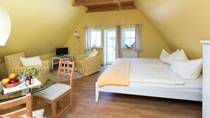 A cozy attic bedroom with a bed, a small table with fruit, a chair, and a sofa.