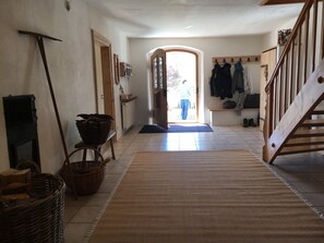 A hallway with a wooden staircase, a radiator, a door leading outside, and a bench with baskets.
