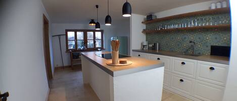 A kitchen with a central island, pendant lights, a window, and a patterned backsplash.