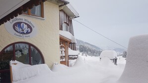 Un edificio con un letrero que dice 'Landhaus Windrose Familie Merz' y alrededores cubiertos de nieve.