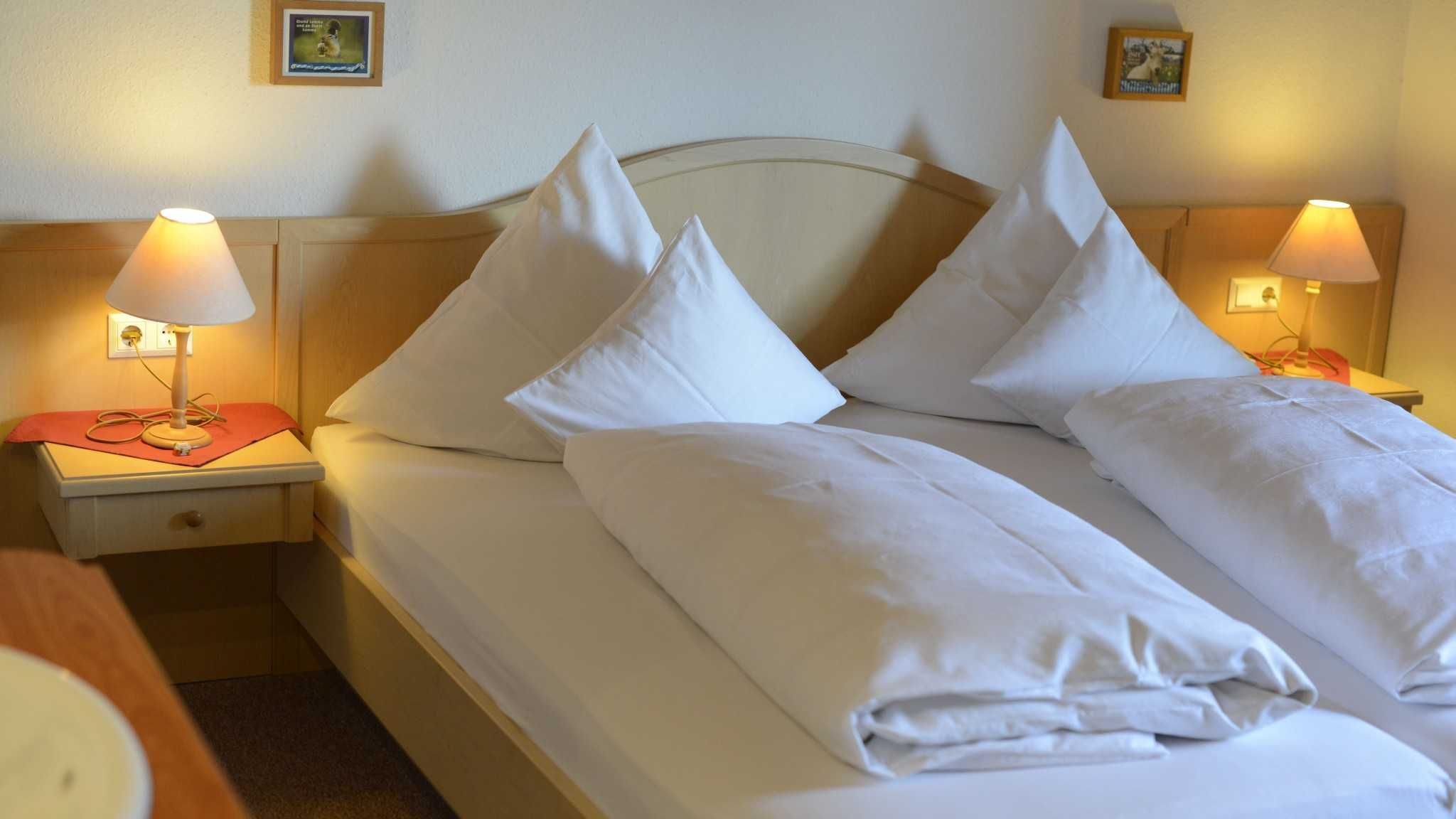 A double bed with white linens, two bedside lamps, and a wooden headboard.