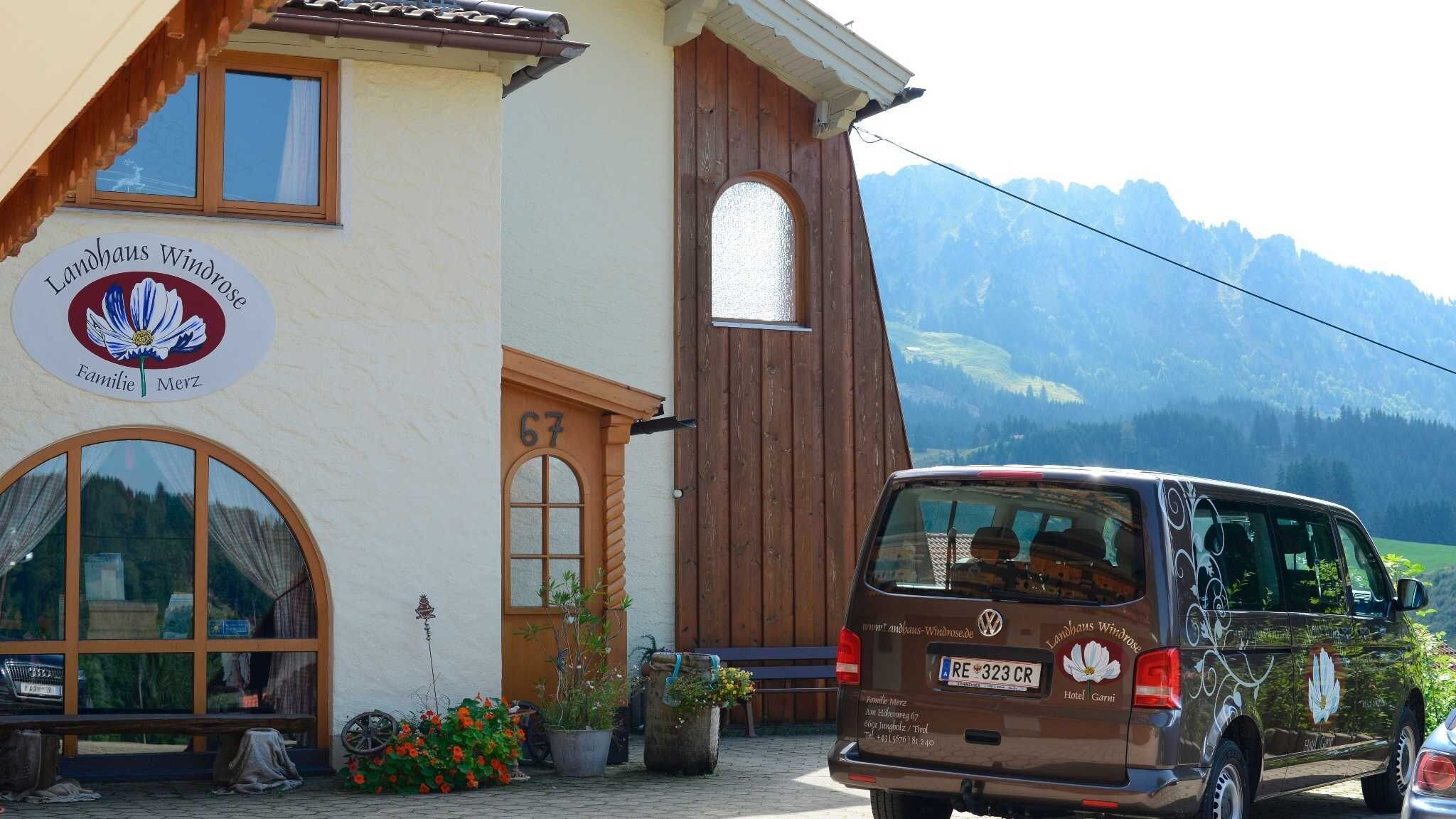 A building with a sign reading 'Landhaus Windrose Familie Merz' and a parked van with a license plate 'RE 323 CR'.