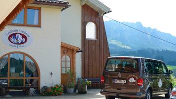 A building with a sign reading 'Landhaus Windrose Familie Merz' and a parked van with a license plate 'RE 323 CR'.