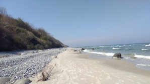 Een kiezelstrand met golven, een heldere lucht en een bebost heuvel.