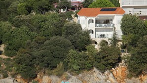 A coastal building with a balcony overlooking the sea, surrounded by dense greenery. - Beach Villa: private bathing area, sandy beach, WiFi, ideal for families (Novalja)