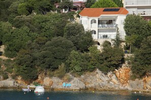 En kystbygning med balkon med udsigt over havet, omgivet af frodig vegetation.