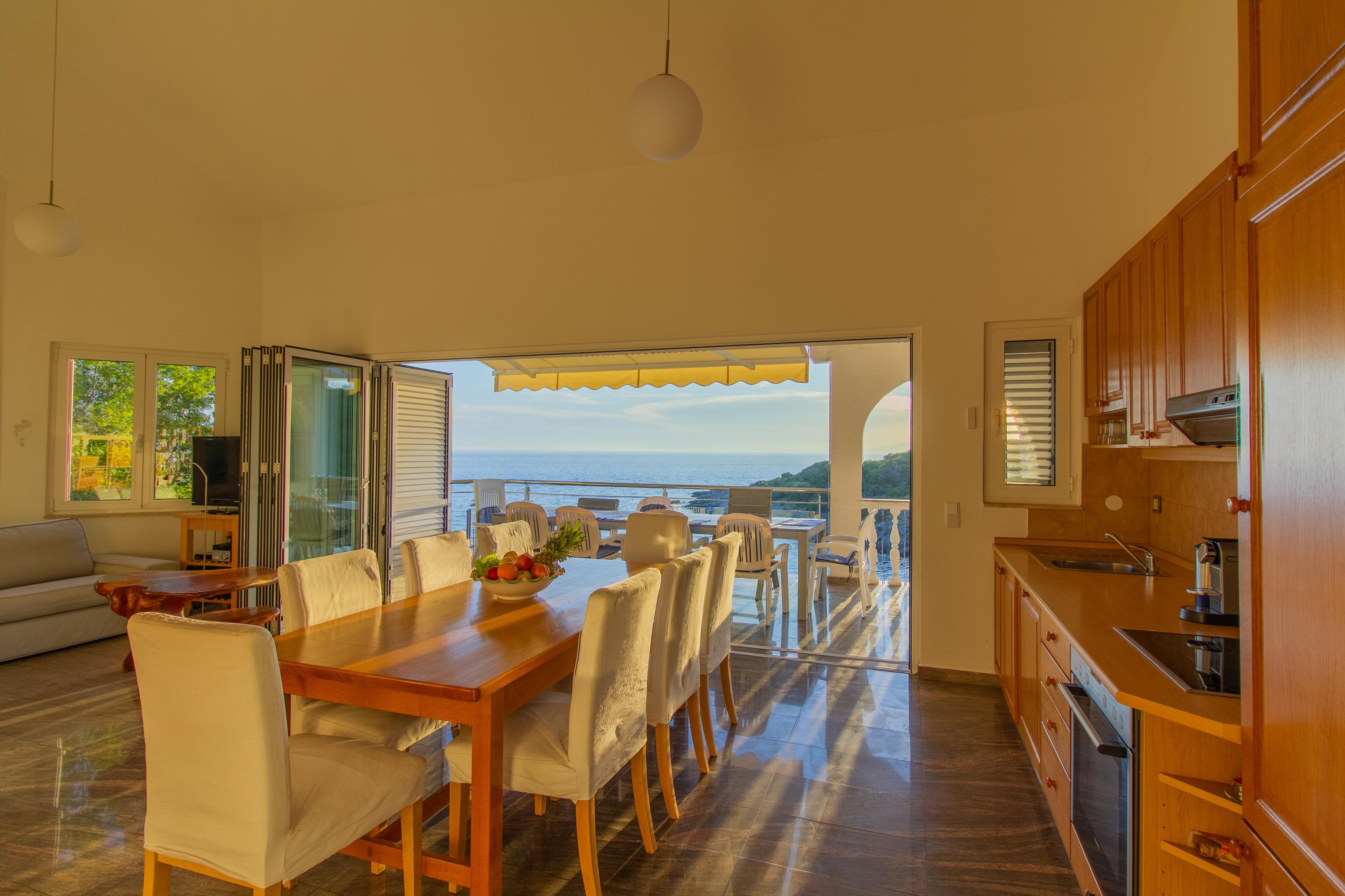 Ein geräumiger Essbereich mit Meerblick, eine Küche mit Holzschränken und ein Balkon mit Tisch und Stühlen.