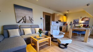 Een moderne woonkamer met een bank, een fauteuil, een salontafel en een eethoek met een tafel en stoelen.