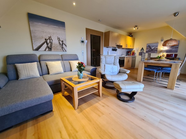A modern living room with a sofa, a chair, a coffee table, and a dining area with a table and chairs.