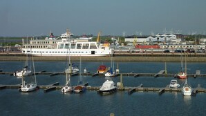 Een jachthaven met diverse boten afgemeerd, een grote witte veerboot en windturbines op de achtergrond.