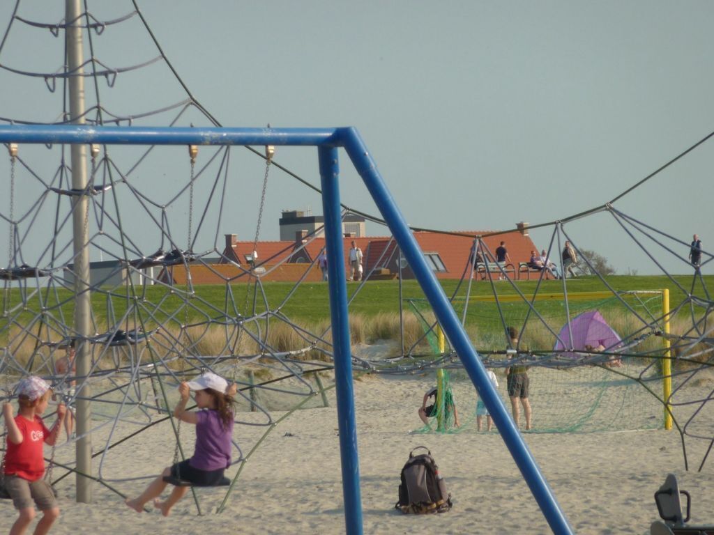 Una spiaggia con un'area giochi delimitata da reti e un edificio sullo sfondo.