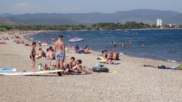 A crowded beach with people sunbathing and swimming.