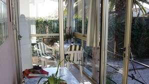 A glass-enclosed patio with a white table, two potted plants, and a white chair.