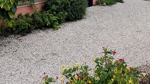 A house with a covered porch, a gravel driveway, and various plants.