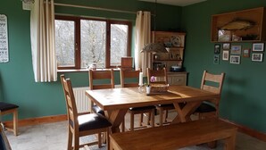 A dining area with a wooden table and chairs, a window with curtains, a shelf with decorative items, and framed pictures on the wall. - Cottage on Lough Ree / River Shannon in the heart of Ireland (Newtowncashel)