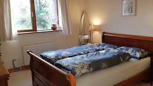 A bedroom with a wooden bed, a window with curtains, a bedside lamp, and a radiator. - Cottage on Lough Ree / River Shannon in the heart of Ireland (Newtowncashel)