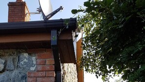 A brick and stone exterior wall with a satellite dish, a wooden deck, and a green shed in a garden setting. - Cottage on Lough Ree / River Shannon in the heart of Ireland (Newtowncashel)
