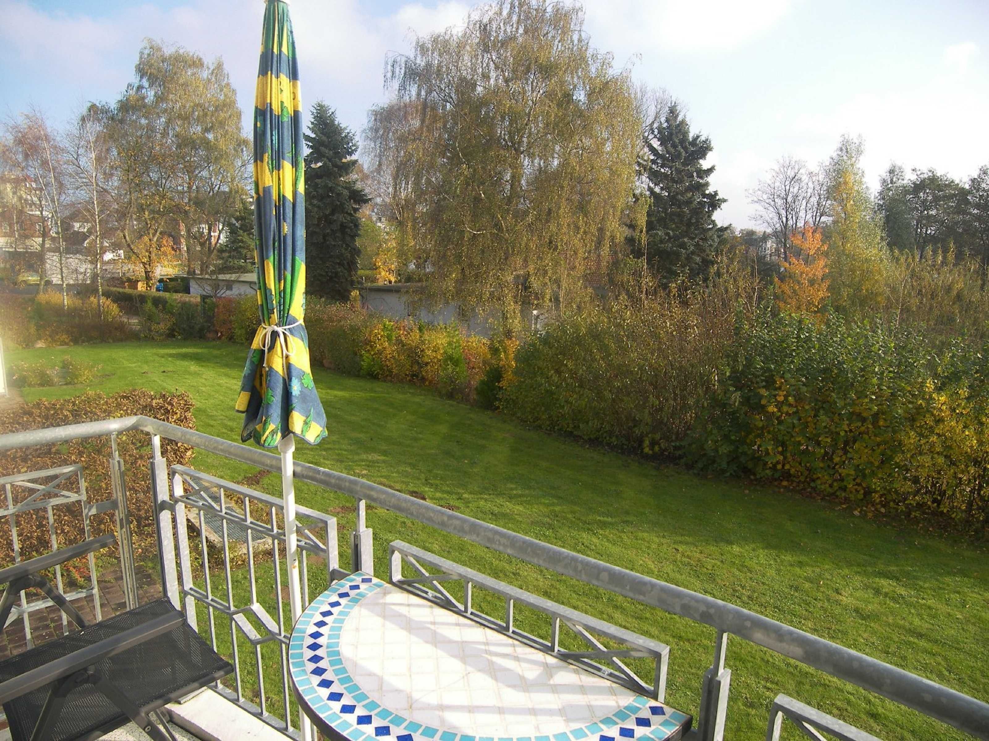Un espace extérieur aménagé en patio, avec une rambarde en métal, une table carrelée et un parasol.