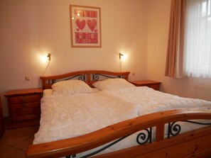 A bedroom with a wooden bed frame, two bedside tables, a nightstand, and a wall-mounted light fixture.