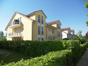 A multi-story yellow building with balconies, surrounded by greenery.