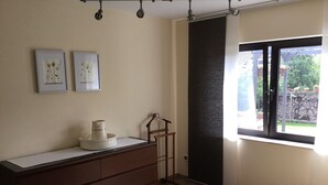 Une chambre avec une commode, une chaise, une fenêtre et deux tableaux accrochés au mur.