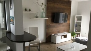 Un salon moderne avec un mur d’accent en bois foncé, un téléviseur à écran plat fixé au-dessus d’une console blanche et un canapé blanc.