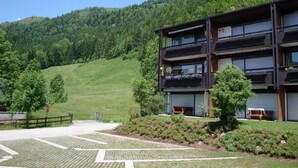 A modern multi-story building with balconies, surrounded by lush green hills and a clear sky. - Luxury 6 pers. Apartment with guest rooms near the golf course and lake (Walchsee)