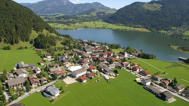 A residential area with houses and a lake, surrounded by mountains. - Luxury 6 pers. Apartment with guest rooms near the golf course and lake (Walchsee)