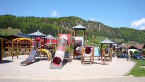 A playground with a slide and climbing structures, set against a backdrop of a mountain and a clear sky. - Luxury 6 pers. Apartment with guest rooms near the golf course and lake (Walchsee)