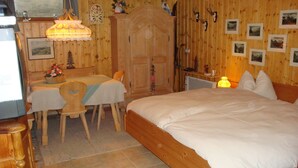 A wooden room with a bed, a table with chairs, a clock, and framed pictures on the wall. - Luxury 6 pers. Apartment with guest rooms near the golf course and lake (Walchsee)