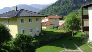 A yellow house with a tiled roof, a stone wall, and a grassy yard. - Luxury 6 pers. Apartment with guest rooms near the golf course and lake (Walchsee)