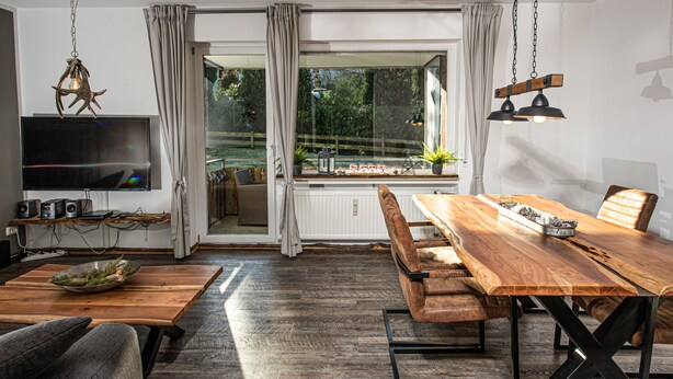 Uma sala de jantar moderna com uma mesa de madeira, bancos e uma televisão numa prateleira.