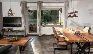 Un espace repas moderne avec une table en bois, des bancs et un téléviseur posé sur une étagère.