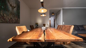 Uma mesa de jantar de madeira com cadeiras, uma luminária pendente e um quadro na parede.