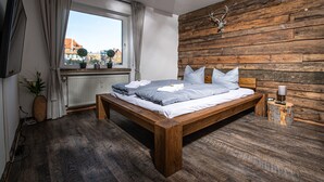 Quarto com cama de madeira, janela com cortinas, cabeça de veado montada e parede de madeira.