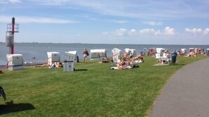 A grassy area with several white RVs and tents, a lighthouse, and a paved walkway along the water.