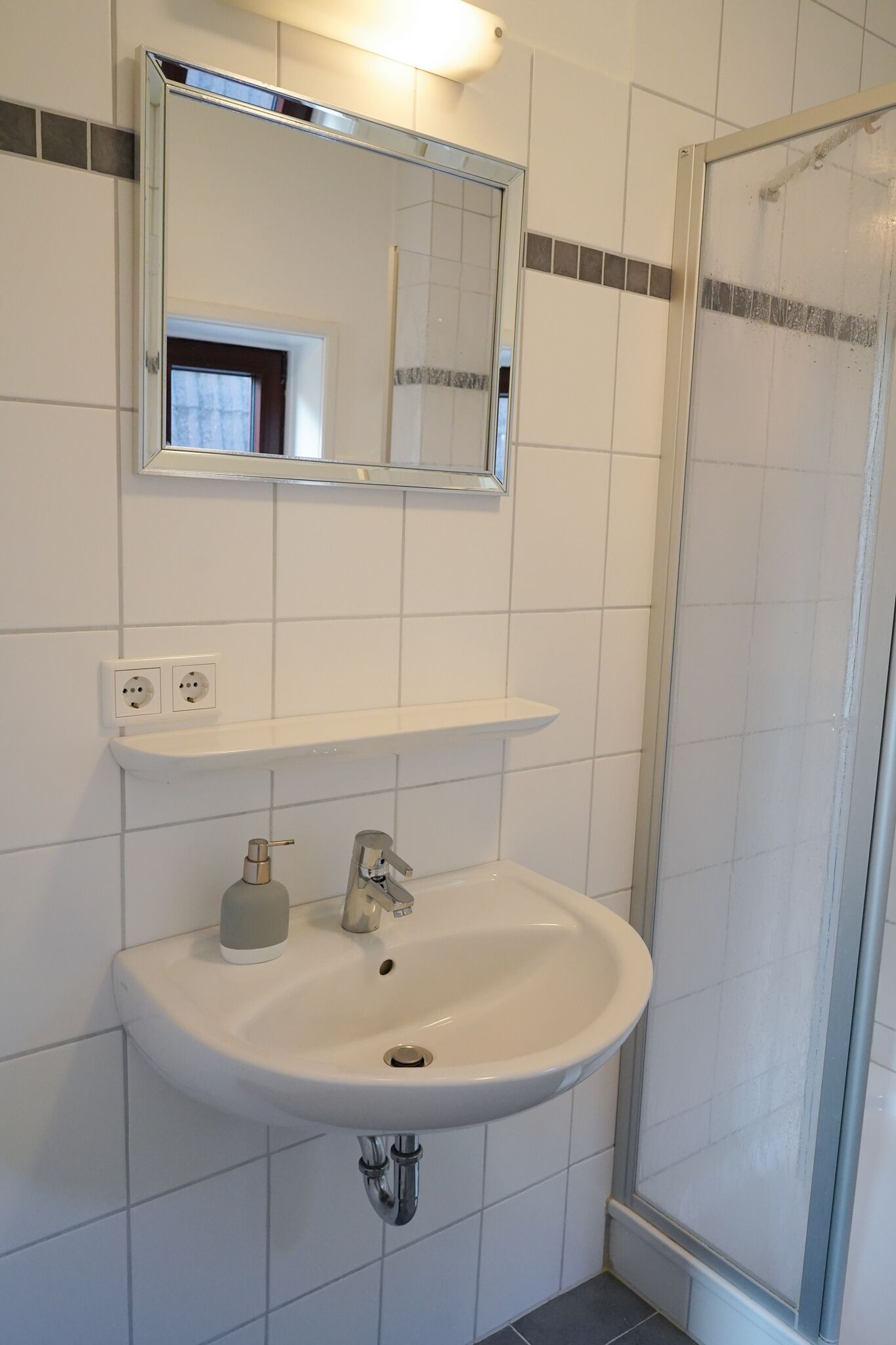 A bathroom with a white sink, a mirror, and a shower enclosure.