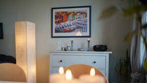 A room with a white dresser, a framed painting of a coastal scene, and a lit candle on the dresser.